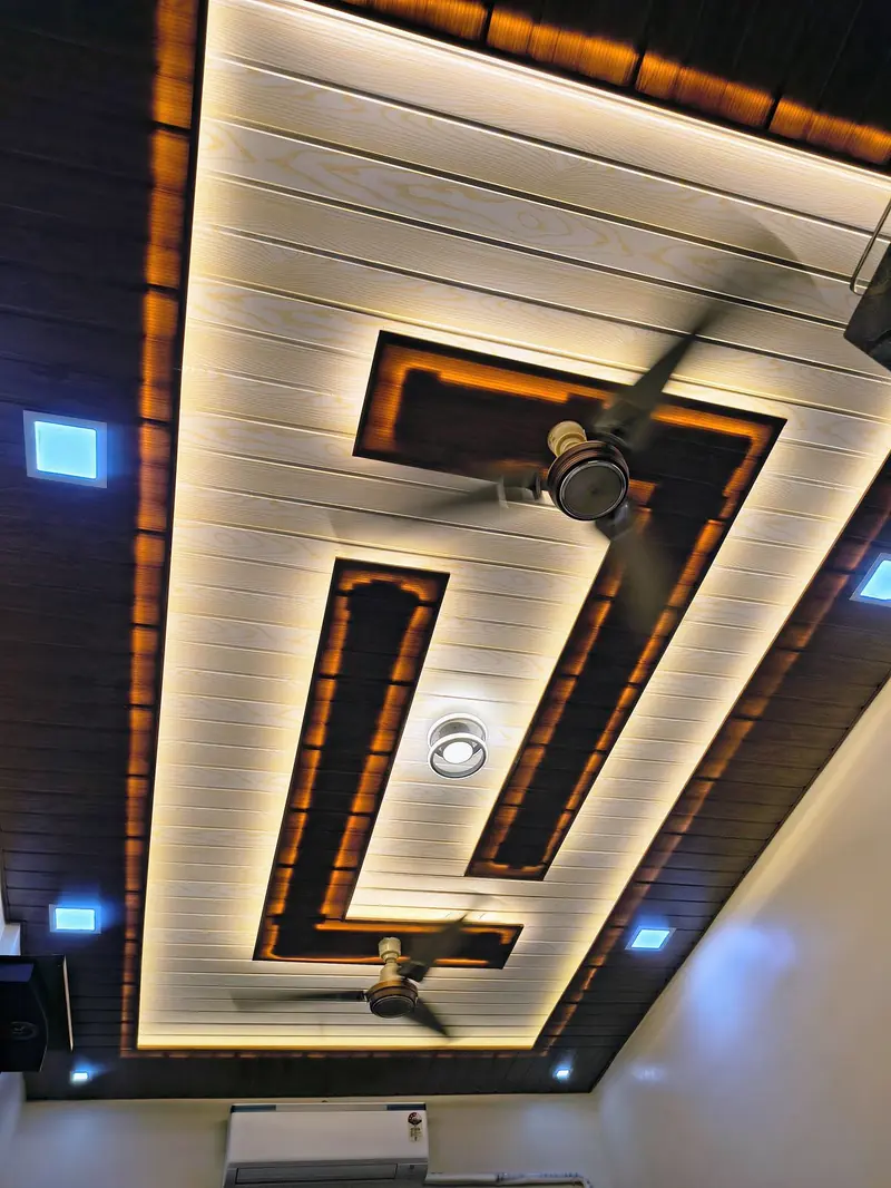 Layered PVC panel false ceiling with warm cove lighting and dark timber-finish borders